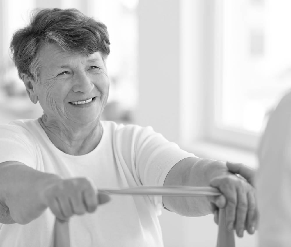 Smiling senior woman doing strength exercise with elastic tape during rehabilitation